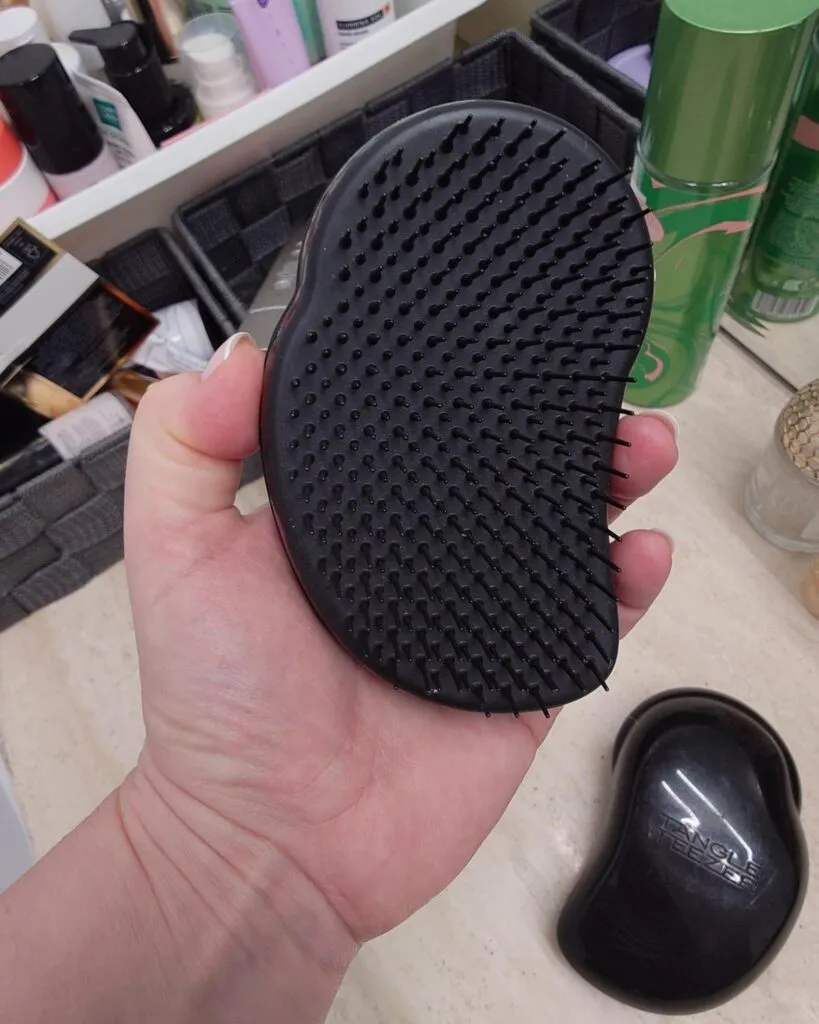 Dłoń trzymająca czarną, nową szczotkę Tangle Teezer The Original, ząbkami do góry. Zbliżenie na elastyczne, polimerowe igły szczotki.