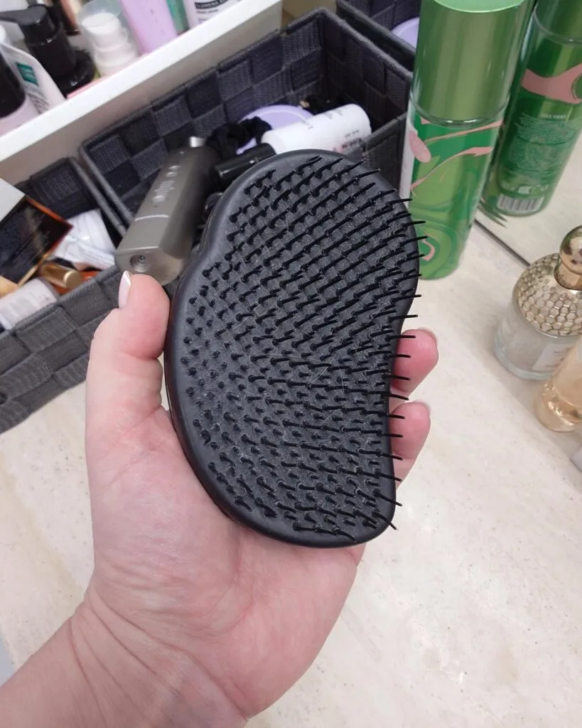 Dłoń trzymająca zużytą, czarną szczotkę Tangle Teezer The Original. Zbliżenie na lekko powyginane polimerowe ząbki po 10 latach używania.