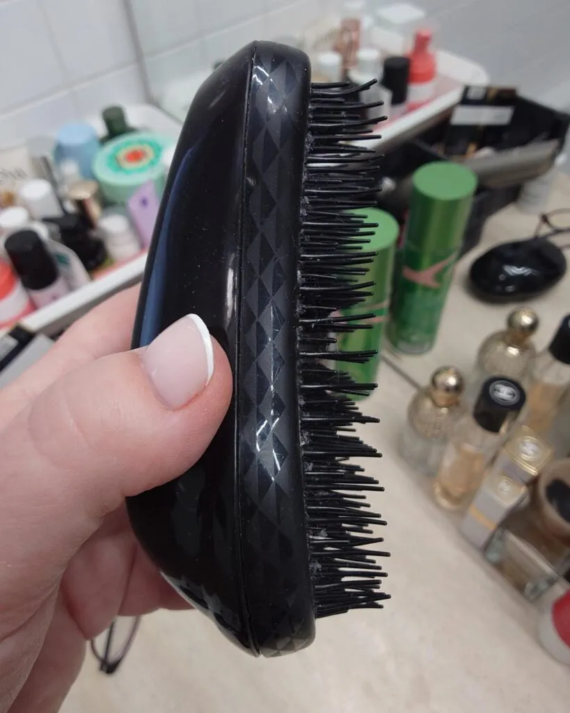 Profil zużytej, czarnej szczotki Tangle Teezer, pokazujący ślady używania i powyginane ząbki na zbliżeniu.